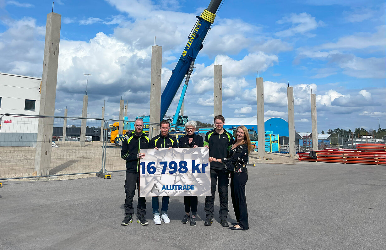 Fem personer ur Alutrades personal h&aring;ller upp skylt med beloppet f&ouml;r &aring;rets vinstdelning, framf&ouml;r byggarbetsplatsen f&ouml;r f&ouml;retagets utbyggnation av lagerlokalerna.